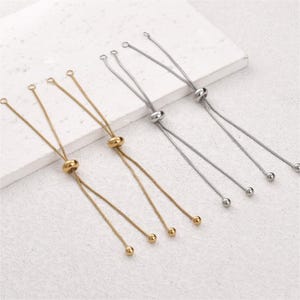 May include: Two gold-toned and two silver-toned adjustable bracelet chains. Each chain features a thin snake-style cord, a sliding bead mechanism for size adjustment, and small spherical end caps on the dangling loose ends of the metal cords.