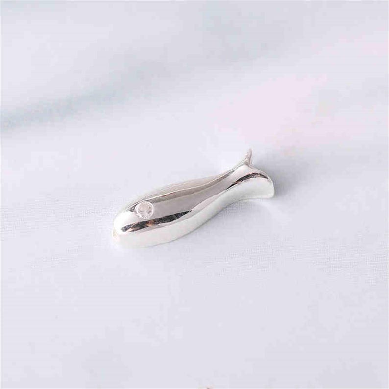 May include: A silver fish charm with a small clear crystal in the centre.