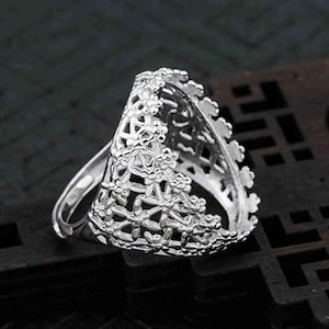 May include: A silver ring with a delicate, floral design. The ring is open in the front, allowing for a stone or other embellishment to be inserted.