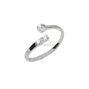 May include: Silver adjustable ring with a bezel setting for a cabochon stone and three clear cubic zirconia stones.