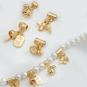 May include: A gold charm bracelet with a variety of charms, including a bee, a flower, a bell, and a tag with Chinese characters. The bracelet is made of white pearls and gold beads.
