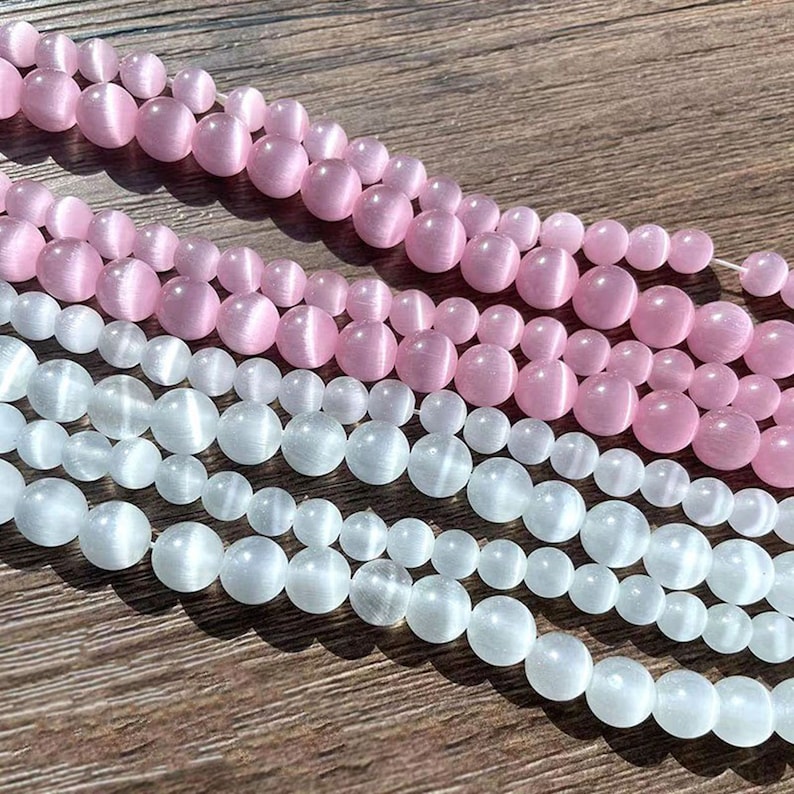 May include: Two strands of round, smooth beads. The top strand is pink and the bottom strand is white. The beads have a subtle shimmer.