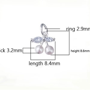 K&ouml;nnte beinhalten: Silberner Anh&auml;nger mit zwei wei&szlig;en Perlenkirschen und klaren Kristallbl&auml;ttern. Der Anh&auml;nger ist 8,4 mm lang, 8,6 mm hoch und 3,2 mm dick. Der Ring hat einen Durchmesser von 2,9 mm.