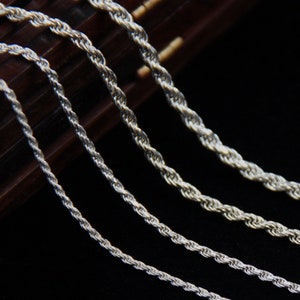 May include: Close-up of several silver rope chains of varying thicknesses. The chains are displayed against a dark background, highlighting their twisted design and metallic sheen. The chains are likely jewelry.