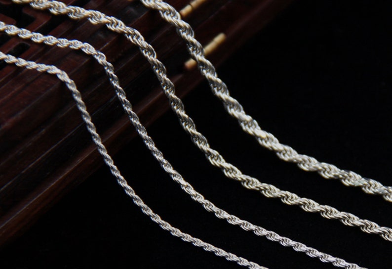 May include: Close-up of several silver rope chains of varying thicknesses. The chains are displayed against a dark background, highlighting their twisted design and metallic sheen. The chains are likely jewelry.