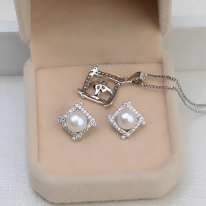May include: A silver necklace and earrings set with a square pendant and earrings featuring a pearl and cubic zirconia stones.