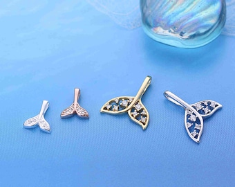 May include: Four different mermaid tail pendants in silver, rose gold, and gold tones, each adorned with sparkling clear crystals. The pendants are arranged on a light blue surface, with a decorative glass stone in the background.