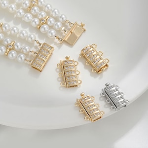 May include: An overhead shot of a three-strand pearl necklace with gold clasps and several gold and silver clasps with embedded clear crystals. The clasps are rectangular with three loops.