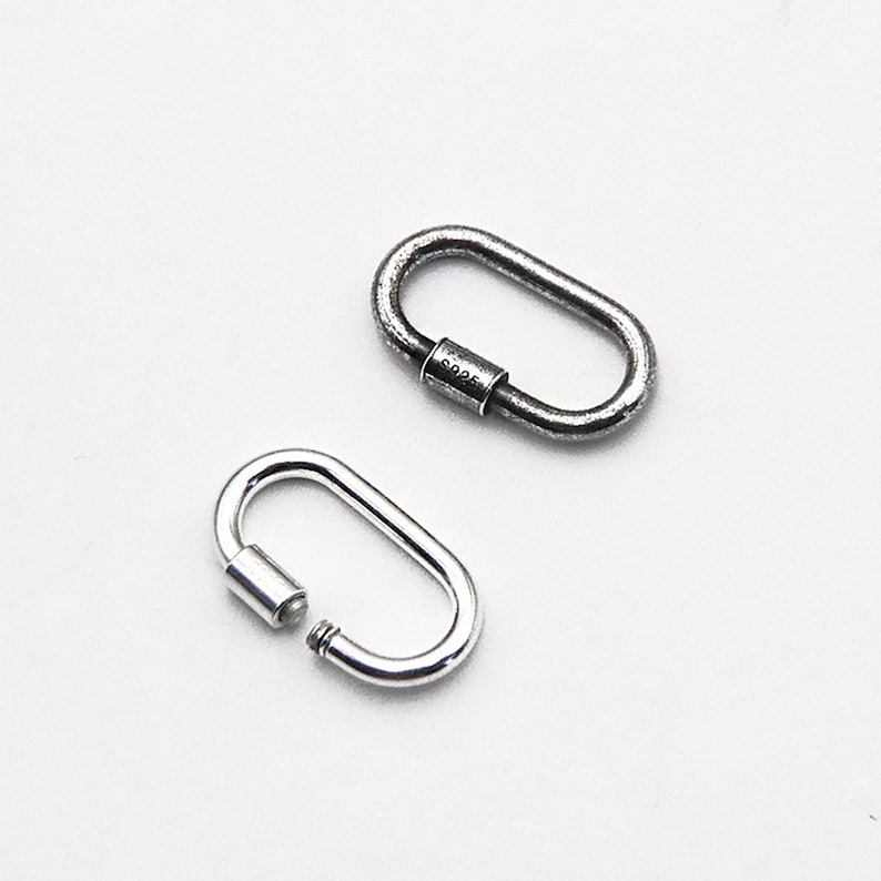 May include: Two oval-shaped, silver-colored carabiner clasps. One clasp is open, revealing the screw mechanism. The other clasp is closed, with the text "S925" visible on the screw barrel. The clasps are on a white background.