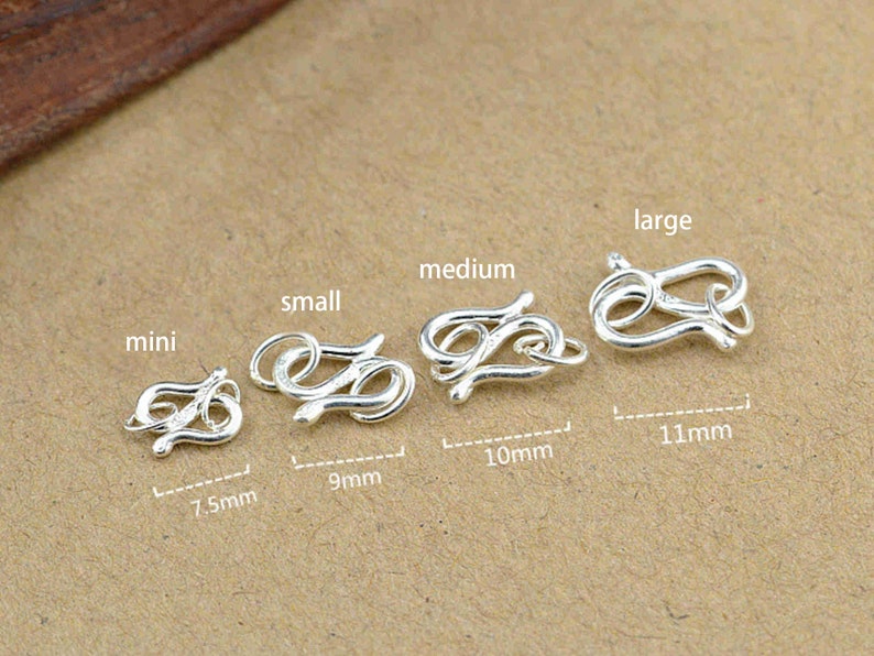 Puede incluir: Cinco cierres de metal plateados en diferentes tama&ntilde;os, etiquetados como "mini", "peque&ntilde;o", "mediano", "grande", con medidas en mil&iacute;metros.