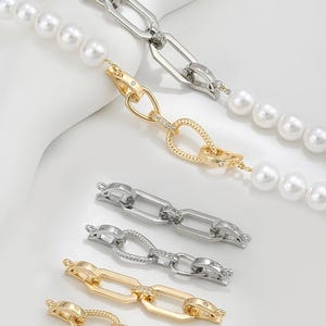 May include: Close-up of jewelry components, including pearl strands and various metal chain links. The links are in silver and gold tones, some with embedded crystals. The pearls are white and round, creating a contrast with the metal.