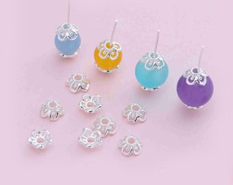 May include: Silver bead caps with a flower design, shown with three different colored glass beads. The bead caps are perfect for jewelry making.