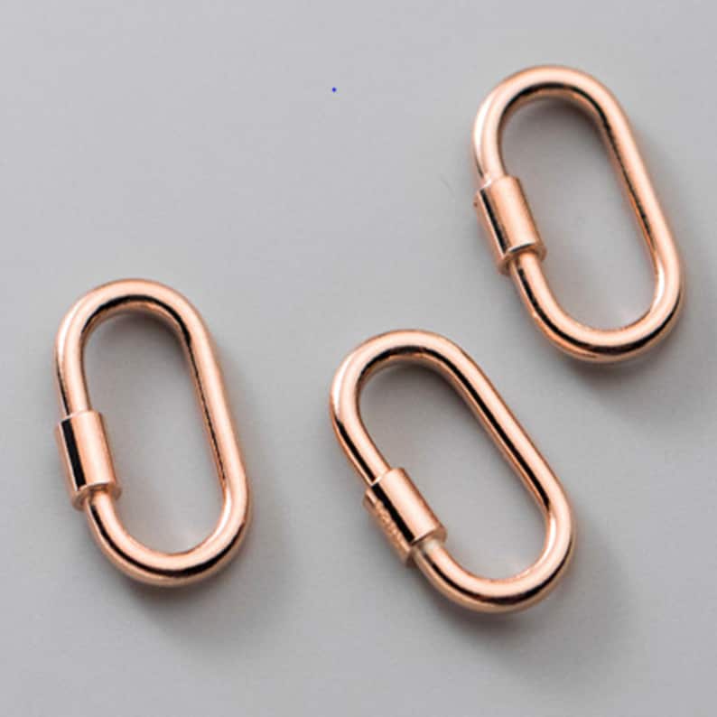 May include: Three rose gold oval-shaped screw lock clasps. Each clasp has a cylindrical screw mechanism in the center. The clasps are displayed on a light gray background.