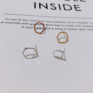 May include: Four pairs of hexagonal stud earrings in gold, silver, and copper. The earrings have a minimalist design. The background includes the word "INSIDE" and text about meditation and praise.