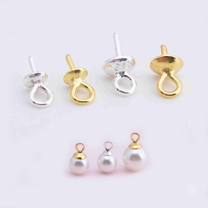 Puede incluir: Una colecci&oacute;n de fornituras para joyer&iacute;a que incluye cuatro enganches met&aacute;licos con pernos en tonos plata y oro, y tres cuentas esf&eacute;ricas blancas con anillas met&aacute;licas integradas en acabados oro y plata, sobre una superficie clara.