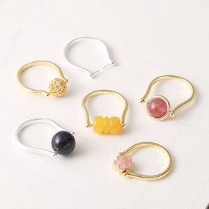Könnte beinhalten: Sechs goldene und silberne Spinnerringe mit verschiedenen farbigen Steinen und Designs. Die Ringe haben ein drehbares Element, wie eine Kugel, einen Zylinder oder eine Blume.
