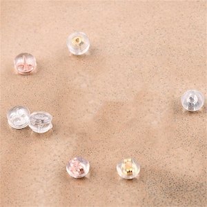 Peut inclure: Gros plan sur un groupe de dos d'oreille en plastique transparent. Les dos sont conçus pour s'adapter au poteau d'une boucle d'oreille et aident à maintenir la boucle d'oreille en place.