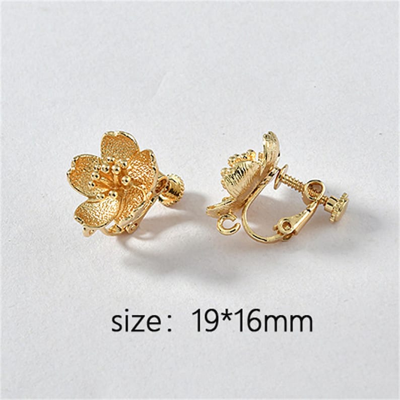 May include: A pair of gold-tone clip-on earrings featuring a flower design. The earrings measure 19mm by 16mm.