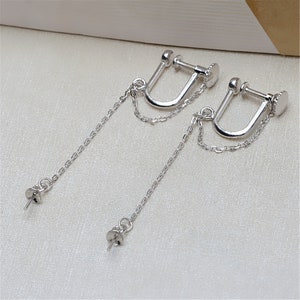 May include: A pair of silver clip-on earrings with a chain dangling from each. The chains are connected to a small silver ball at the end.
