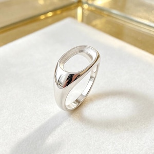May include: A polished silver ring with an oval-shaped setting. The ring has a smooth, reflective surface and a simple, elegant design. The setting is open, ready for a gemstone or other embellishment.