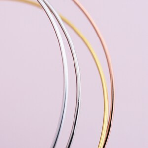 May include: Three thin metal hoops in silver, gold, and rose gold, arranged in a circle on a pink background.