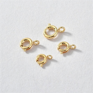 May include: Four gold-toned metal jump rings of varying sizes. The rings are open and have a small loop on one side.
