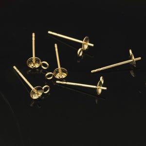 Puede incluir: Hallazgos de pendientes de color dorado con un bucle y una base plana redonda. Los hallazgos están dispersos sobre una superficie negra.