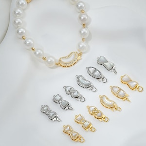 May include: A set of 10 pearl and rhinestone jewelry clasps in silver and gold tones. The clasps are in various shapes, including hearts, bows, and crescent moons.