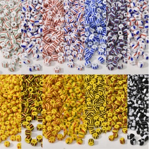Pode incluir: Conjunto de contas de vidro coloridas com listras brancas. As contas estão dispostas em filas, cada fila com uma combinação de cores diferente. As cores incluem verde, vermelho, azul, amarelo, preto e branco.