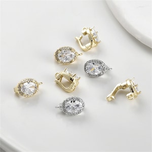 May include: Six gold and silver tone oval-shaped pendant clasps with clear crystal accents. Each clasp has a hinged opening and a loop for attaching a chain or cord.