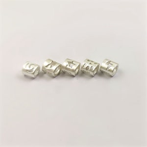 May include: Five silver charm beads with different cut-out designs. The beads are arranged in a row on a white surface.