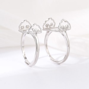 May include: Two silver rings featuring a cloud motif. The rings have an adjustable band and a decorative cloud design at the top, with a swirling pattern. The rings are set against a white backdrop.
