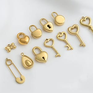 Puede incluir: Un conjunto de dijes de metal dorado con una variedad de formas, incluyendo corazones, llaves, candados, una mariposa y un pasador de seguridad.