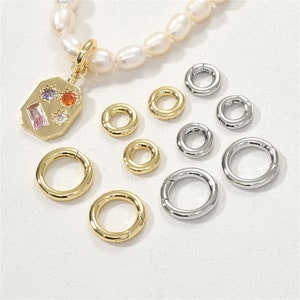 May include: A collection of jewelry components, including gold-toned and silver-toned spring ring clasps and a gold pendant with colorful gemstones. A pearl necklace is also present. These components are used for jewelry making.