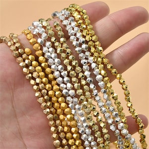 May include: A strand of gold and silver faceted beads. The beads are small and have a geometric shape. The beads are strung on a clear thread.