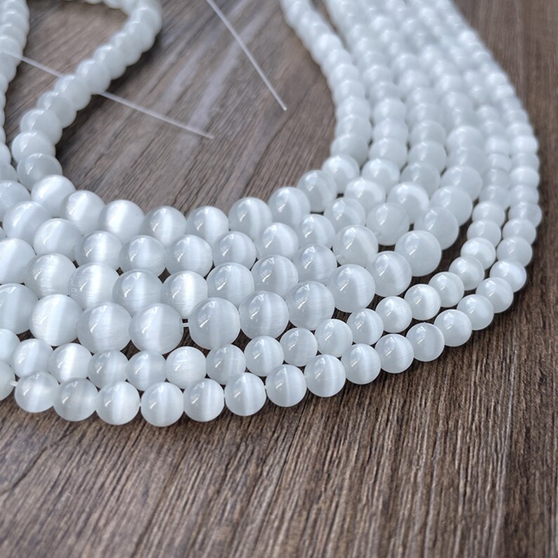 May include: A strand of white cat's eye beads. The beads are round and have a smooth, polished finish. They are strung on a clear thread.