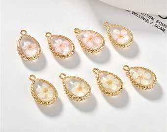 May include: Ten gold-tone teardrop-shaped pendants with a clear resin filled with dried flowers. The flowers are pink and white.