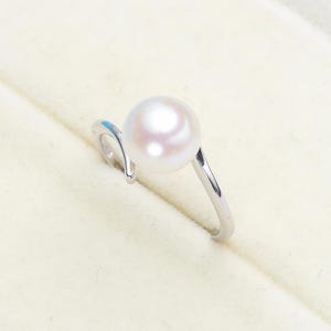 May include: A silver ring with a white pearl set in a curved band.