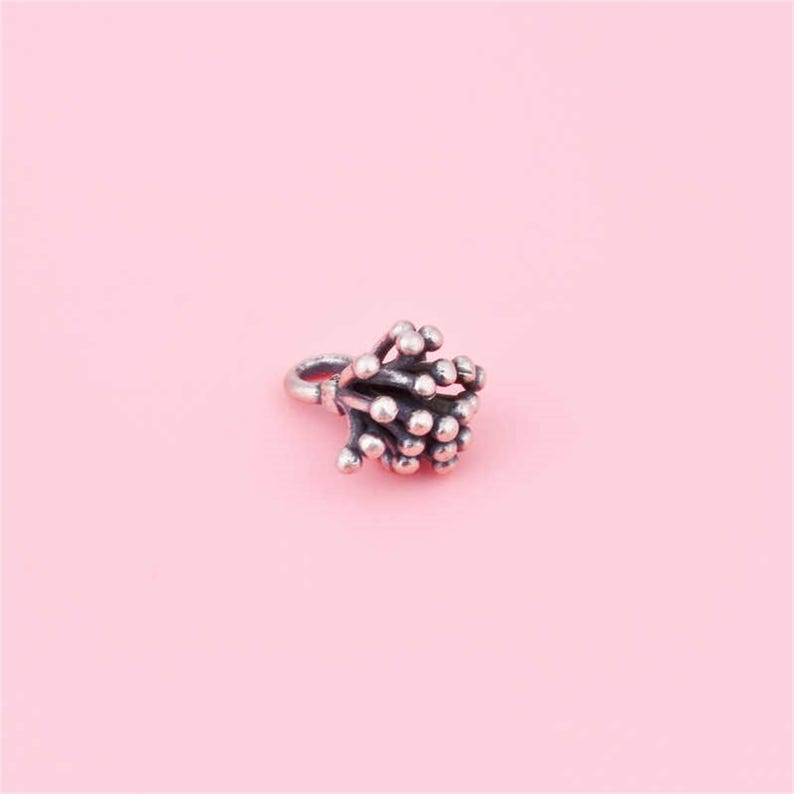 May include: A silver charm in the shape of a flower with a loop for attaching to a bracelet or necklace.