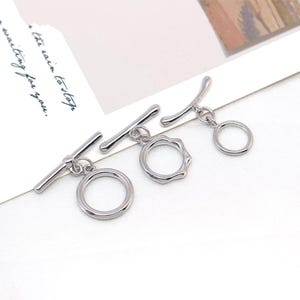 May include: Three silver toggle clasps. Each clasp has a bar and a ring, with one ring having a wavy design. The clasps are displayed on a white surface. The image includes the text, "the rain to stop, waiting for you."