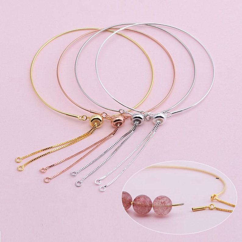 May include: Four adjustable bracelets with a sliding bead and chain. The bracelets are available in gold, rose gold, and silver. The bracelets are shown on a pink background.