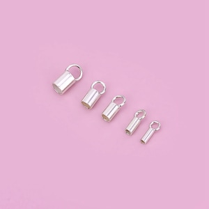 May include: Five silver-toned metal end caps for jewellery making, arranged in order of size from largest to smallest on a pink background.
