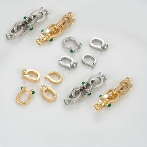 May include: An assortment of jewelry clasps and connectors in gold and silver tones. Some clasps feature clear and green gemstones. The clasps are in various shapes and sizes, suitable for necklaces and bracelets.