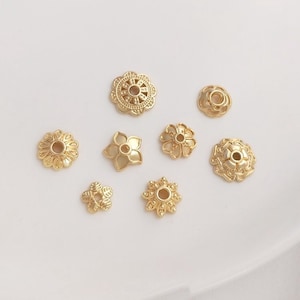 Könnte beinhalten: Acht goldfarbene Metallperlenkappen mit filigranen Blumenmustern. Die Kappen haben ein Loch in der Mitte zum Einfädeln.