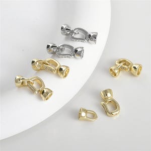 May include: A set of six gold and silver metal clasps with a decorative design. The clasps are used for jewelry making.