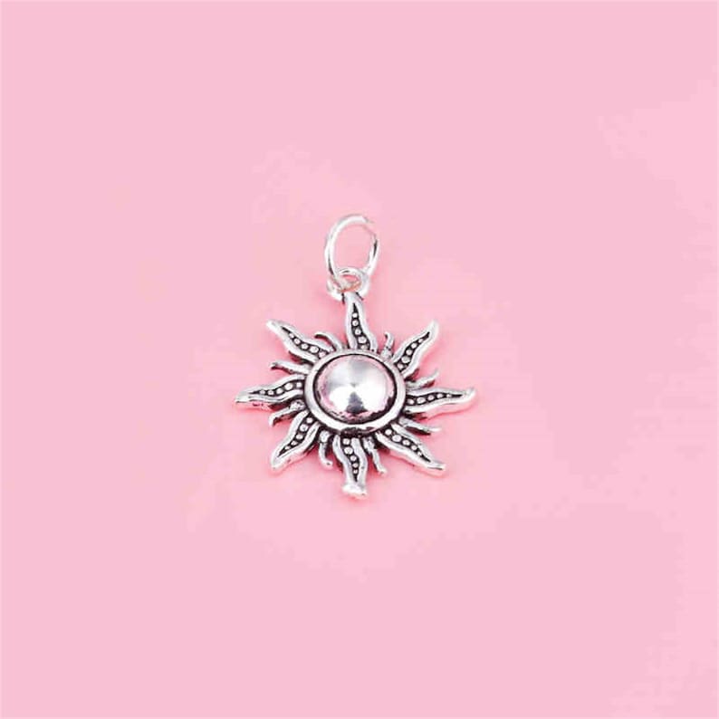 Puede incluir: Un colgante de sol de plata con un dise&ntilde;o detallado. El sol tiene un centro redondo y rayos que se extienden hacia afuera.