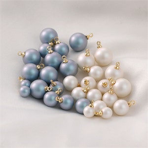 Op de afbeelding: Een verzameling parels en blauwe glazen kralen met goudkleurige dopjes. De kralen zijn in een halve cirkel op een wit oppervlak gerangschikt.