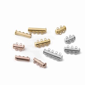 May include: A collection of multi-strand tube clasps for jewelry making, featuring cylindrical designs in gold, silver, and rose gold tones. Each clasp includes multiple small circular loops for attaching jewelry strands, with varying lengths and loop counts.