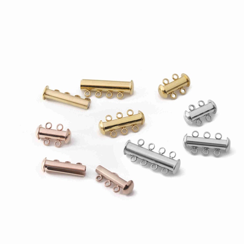 May include: A collection of multi-strand tube clasps for jewelry making, featuring cylindrical designs in gold, silver, and rose gold tones. Each clasp includes multiple small circular loops for attaching jewelry strands, with varying lengths and loop counts.