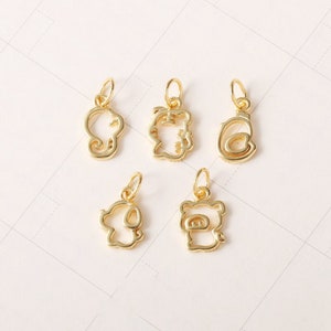May include: Five gold-coloured metal charms in the shape of a cat, pig, elephant, dog, and a swirl. The charms are all outlined and have a hollow centre.